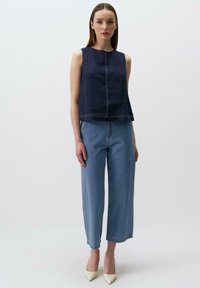 Top senza maniche di colore blu navy con scollatura rotonda e cuciture in contrasto, abbinato a jeans a gamba larga di un azzurro chiaro e tacchi bianchi a punta.