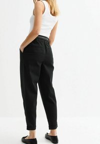 Svarta, figursydda byxor med hög midja, sidofickor och rullade fållar. Kombineras med en vit linne och svarta platta skor. Slät tygtextur.