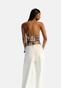 Top sans bretelles à motif marron, cintré au niveau de la poitrine, associé à un pantalon large blanc avec poches arrière. Tissu lisse, accents minimalistes.