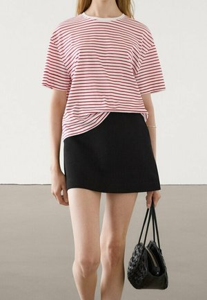 Woman wearing a red and white striped short-sleeve shirt and black mini skirt, holding a small black handbag with a braided design.