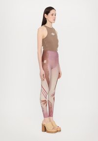 Brown sleeveless top with a diamond cutout; pink and beige leggings featuring floral patterns; tan wooden platform sandals.