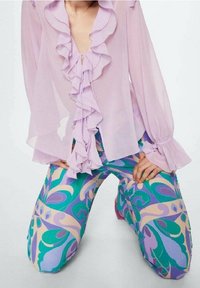 Jasnofioletowa, przezroczysta bluzka z falbanami z przodu i szerokimi rękawami. Połączona z wzorzystymi spodniami w zielone, fioletowe i beżowe wiry.