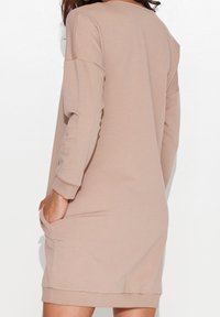 Długa beżowa sukienka z długim rękawem, wykonana z miękkiego materiału, o luźnym kroju, z okrągłym dekoltem i bocznymi kieszeniami. Gładka faktura z prążkowanymi mankietami.
