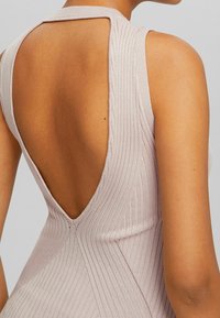 Robe sans manches rose clair avec un dos en V profond, texture côtelée et design ajusté ; tissu doux avec des détails de couture subtils.