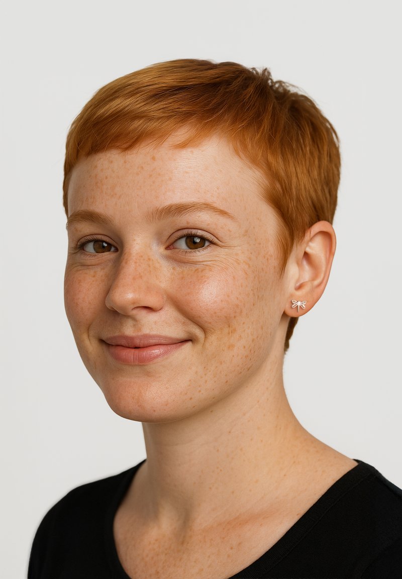 Silverfärgad örhänge i form av en fjäril, buren av en person med kort rött hår och fräknar, mot en neutral bakgrund som framhäver örhängets detaljer.