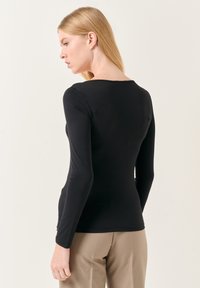 Top nero a maniche lunghe con scollo rotondo e silhouette aderente, realizzato in tessuto elasticizzato. Abbinato a pantaloni beige chiaro.