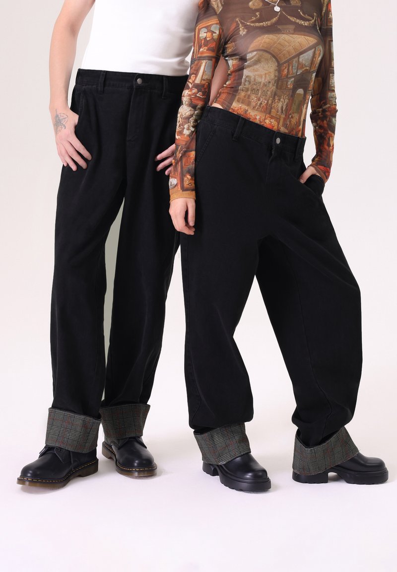 Pantalones anchos negros de cintura alta y puños con un patrón a cuadros en verde. Combinados con zapatos de cuero negros. Con bolsillos visibles y un cierre de botón.