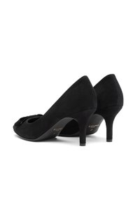 Scarpe con tacco kitten in suede nero con un piccolo dettaglio a fiocco sulla parte anteriore, inclinate per mostrare i lati e i tacchi su uno sfondo bianco.