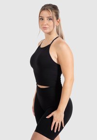 Conjunto deportivo negro que incluye una camiseta ajustada con tirantes finos y pantalones cortos de ciclismo de cintura alta, ambos en una tela elástica y suave.