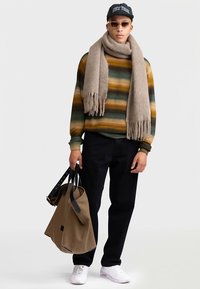 Gestreepte trui in groen, geel en bruin; beige sjaal met franjes; zwarte broek; bruine tote met donkere bandjes; witte sneakers; zwarte pet.
