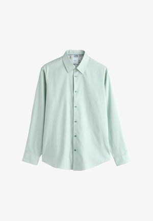 Hele roheline pikkade varrukatega särk, millel on nööbitav esikülg ja terava kraega kaelus, kaeluse sees on lillemustriga ja särk on valgel taustal laotatud.