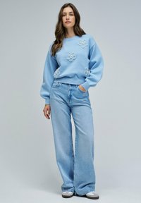 Suéter azul claro con bordado floral, cuello redondo y mangas largas, combinado con unos jeans de denim de tiro alto y pierna ancha.