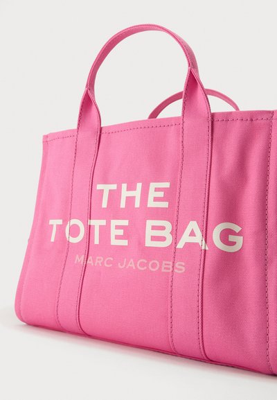 Sac fourre-tout en toile rose vif avec des poignées courtes et un texte blanc indiquant "THE TOTE BAG MARC JACOBS" sur le devant.