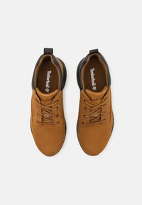 Scarpe in suede marrone con accenti neri, punta rotonda e chiusura con lacci. Presentano un interno imbottito e una suola in gomma testurizzata.