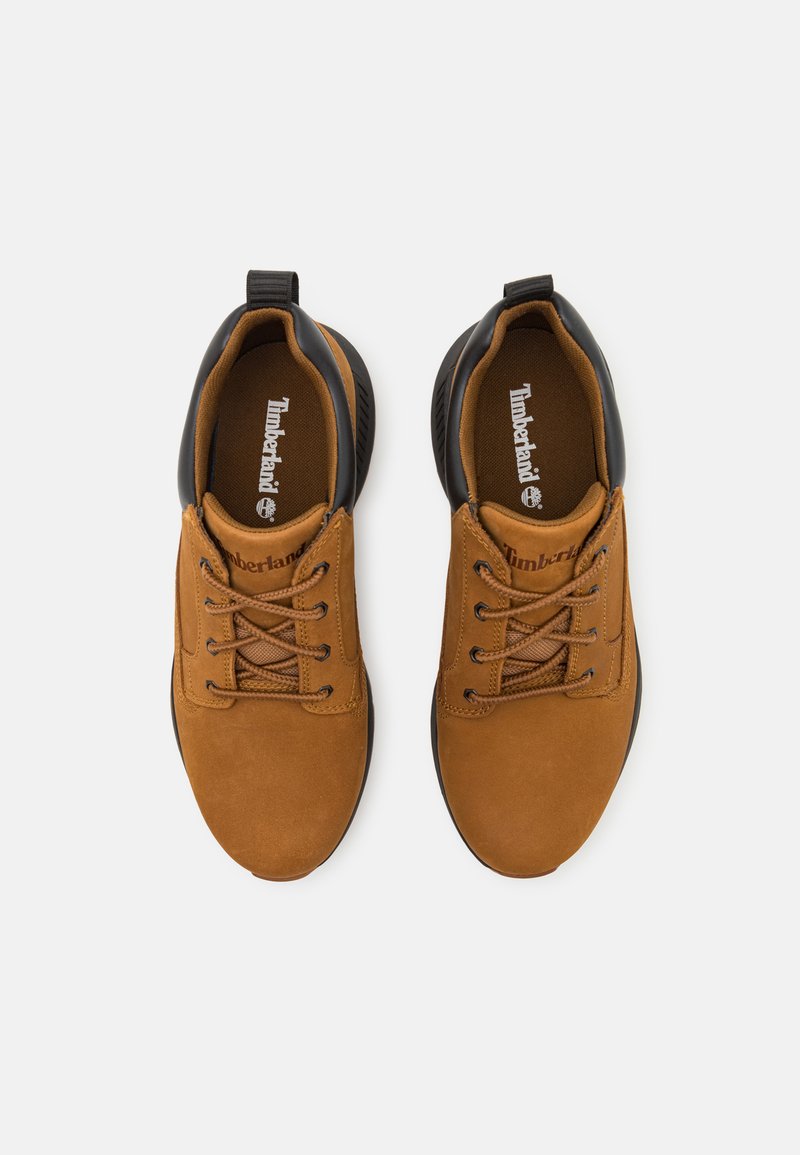 Bruine suède schoenen met zwarte accenten, ronde neus en vetersluiting. Beschikt over een gevoerde binnenkant en een textuur rubberen zool.