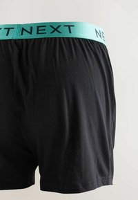 Fekete boxeralsó világoskék derékszíjjal, amelyen a "NEXT" felirat található fekete betűkkel. Puha, sima anyagból készült, laza szabással.