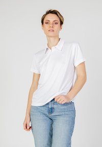 Polo bianco con maniche corte, design con collo, caratterizzato da un logo discreto. Abbinato a jeans in denim azzurro chiaro. Texture liscia.