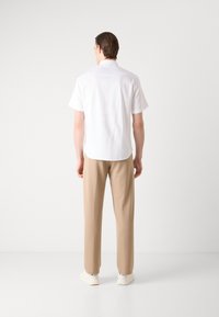 Camicia bianca a maniche corte con orlo dritto e una texture morbida, abbinata a pantaloni beige e scarpe chiare.