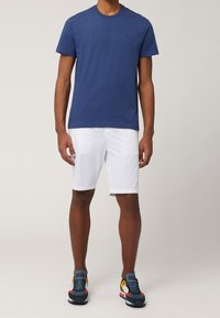 Marineblå t-shirt i bomuld kombineret med hvide shorts og flerfarvede sneakers. T-shirten har rund hals og diskrete logodetaljer.