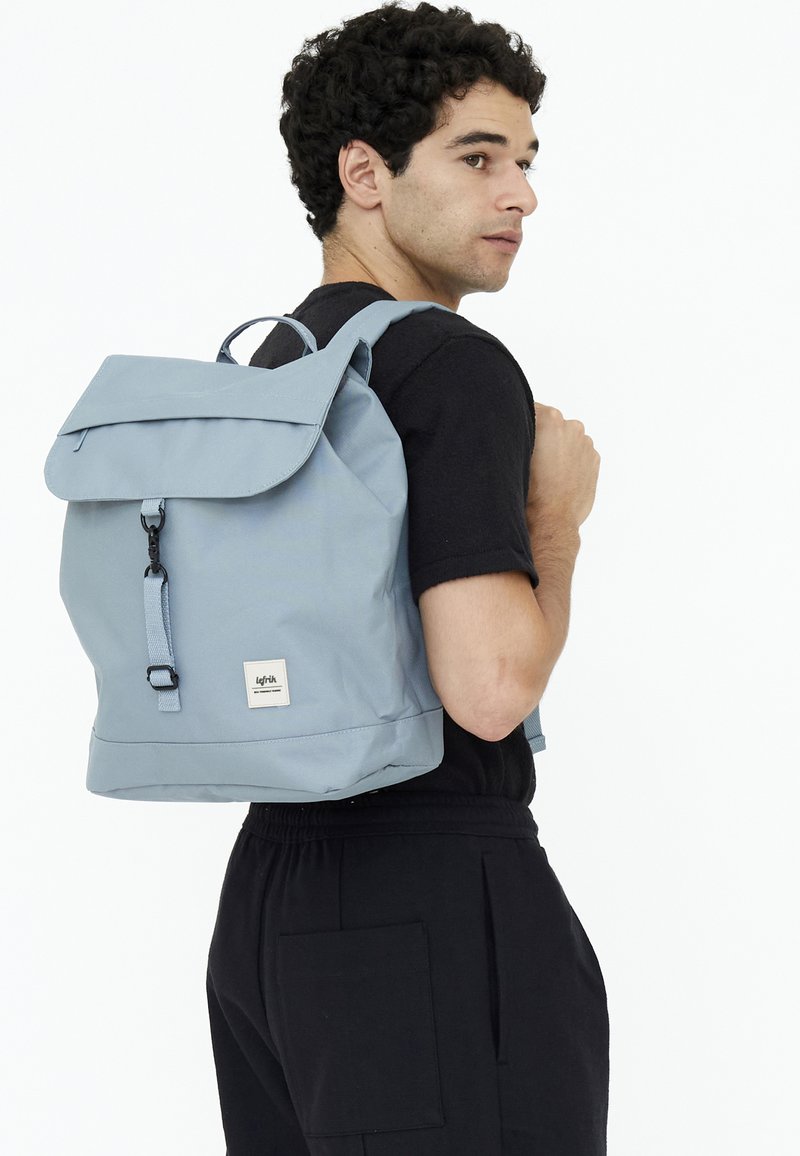 Ljust blå ryggsäck med vikbar klaff, justerbara axelremmar och ett frontspänne. Tillverkad av hållbart material med en kvadratisk botten och logopatch.