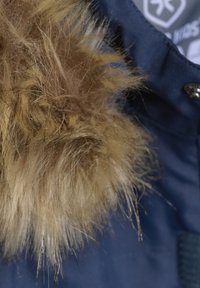 Marinblå jacka med fuskpälsdetaljer; fluffig textur i ljusbrunt och beige som kontrasterar mot den blåa tygbakgrunden.