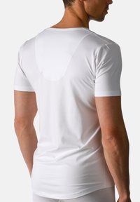 Mand iført en enkel hvid kortærmet tætsiddende T-shirt set fra ryggen mod en ensfarvet baggrund.
