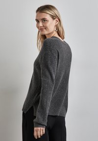 Mörkgrå ribbad stickad tröja med avslappnad passform, sidoflikar och långa ärmar, som visar en mjuk textur och avslappnad design.