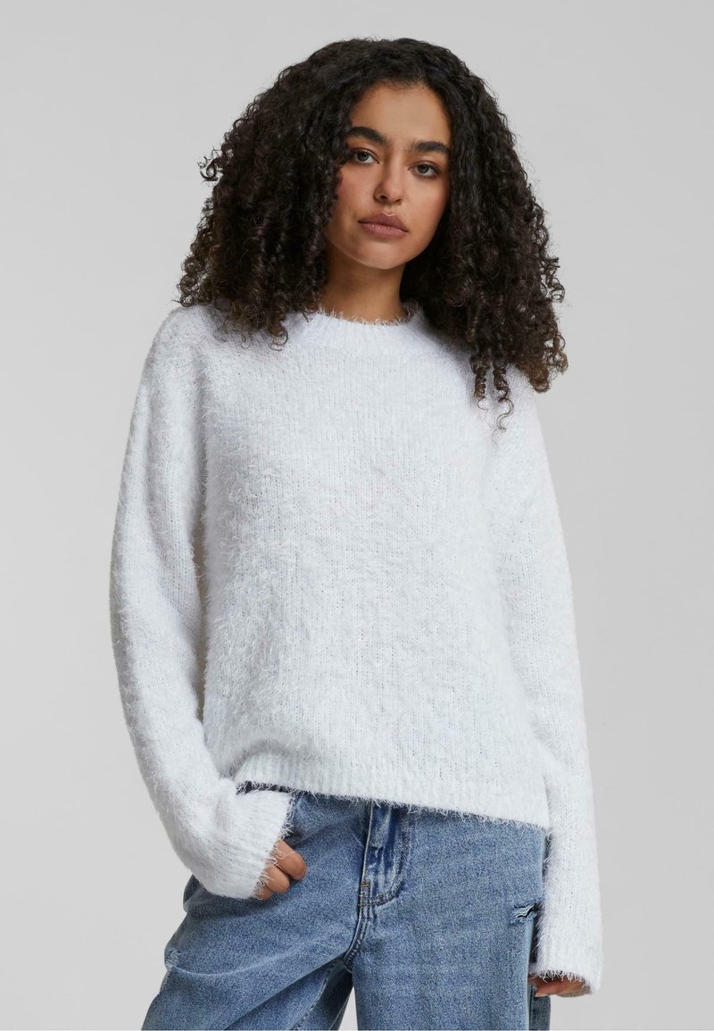 Maglione bianco e soffice con scollo rotondo e tessuto lavorato. Presenta maniche lunghe e una vestibilità rilassata, abbinato a jeans blu.