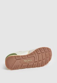 Zapatilla deportiva con suela de goma marrón, paneles verdes y beige, textura similar al cuero y logo en relieve en el costado.