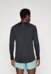 Langærmet sort sports T-shirt med en glat overflade, der har en rund halsudskæring og små ventilationshuller på bagsiden. Inkluderer turkise shorts.