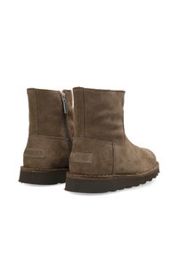 Botas de ante marrón hasta el tobillo con una textura suave, que presentan cremalleras laterales y suela de goma. Logo de la marca visible en la parte trasera.