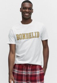 Vit bomulls-t-shirt med texten "BONDLEDID" tryckt i gula, feta bokstäver, kombinerad med röda och vita rutig dragsko-shorts.