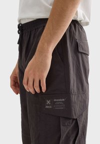 Svarta cargo-shorts med lätt material, elastisk midja och flera fickor. Har en logotag på den nedre sidan.