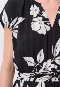 Czarna bluzka z białym kwiatowym wzorem, z dekoltem w kształcie litery V, krótkimi rękawami, marszczonym pasem i strukturalnym materiałem.