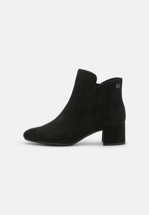 Schwarzer Veloursleder-Ankle-Boot mit Blockabsatz, runder Zehenpartie und seitlichem Reißverschluss, dargestellt vor einem einfarbigen hellgrauen Hintergrund.