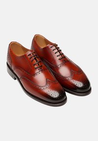 Braune Leder-Brogues mit klassischem Wingtip-Design, gestanzten Musterakzenten und einer polierten schwarzen Zehenkappe. Mit Schnürverschluss.