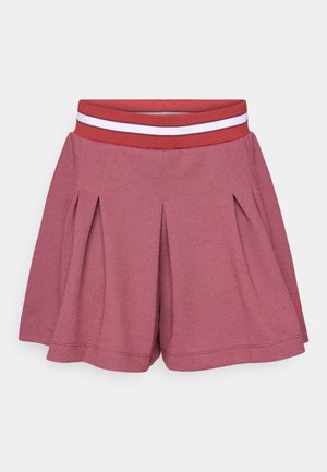 Vaaleanpunaiset laskostetut shortsit, joissa on leveä punainen vyötärönauha, jossa on valkoinen vaakasuora raita, esillä valkoisella taustalla.