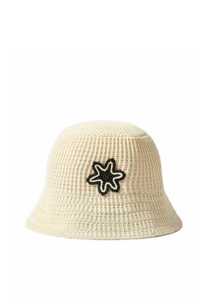 Sombrero tipo bucket color crema tejido a crochet con un parche de flor delineado en negro y blanco en la parte delantera.