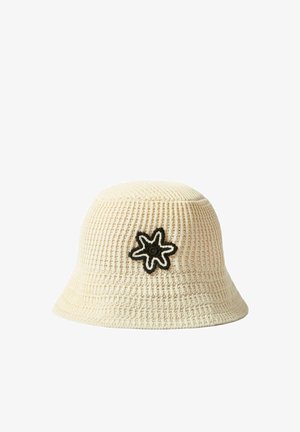 Cappello a secchiello color crema all’uncinetto con toppa a fiore contornata in bianco e nero sul davanti.