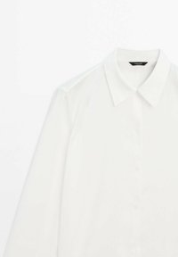 Chemise blanche à manches longues avec un col classique, une fermeture à boutons et un tissu lisse et léger à la texture subtile.