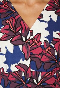 Vestido de estampado floral con grandes flores moradas y rojas sobre un fondo azul y blanco, con un diseño de escote en V y textura suave.