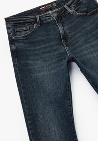 Vaqueros rectos de denim de color azul oscuro, con un diseño clásico de cinco bolsillos, costuras visibles y un cierre de botón.