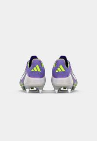 Purple and yellow soccer cleats with a sleek design, transparent sole, and heel accents. Features three distinct stripes on the back.