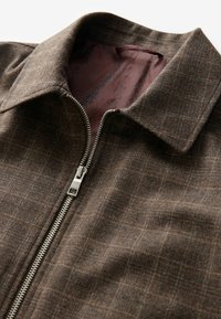 Brown plaid jacket with a smooth texture, featuring a front zipper, a collar, and a maroon patterned lining.