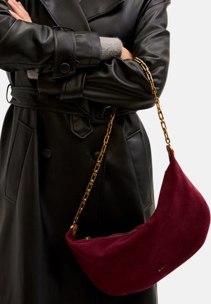 Burgunderfarbene Wildleder-Umhängetasche mit einer goldenen Kettenriemen, geschwungenem Design und einem Reißverschlussverschluss, mit einem eingeprägten Logo auf der Vorderseite.