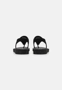 Sorte flip-flops med flat såle, med et strukturert stroppdesign og et minimalistisk silhuett. Fotbedet har en subtil merkevaredetalj.