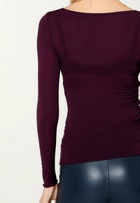 Tiefviolettes Langarmshirt mit Boot-Ausschnitt und gerafftem Seitennähendetail, gefertigt aus einem glatten, elastischen Stoff.