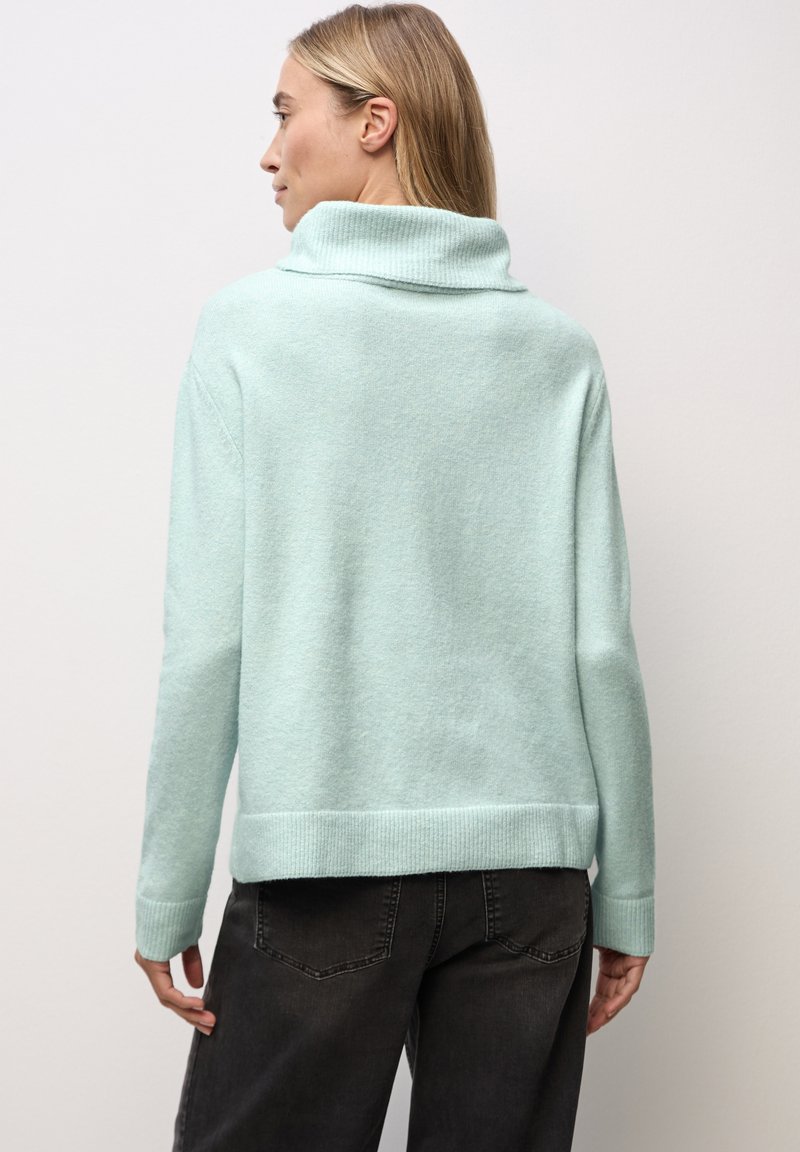 Miętowy sweter z prążkowanym golfem, miękka faktura i obniżone ramiona. Połączony z ciemnymi dżinsami, prezentującymi luźny krój.