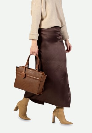 Žena v béžovém svetru a hnědé saténové sukni, držící texturovanou hnědou kabelku, kráčející v béžových kotníkových botách na podpatku.