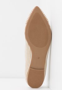 Randig skosula i beige och vitt med en spetsig form. Har en strukturerad gummibotten för grepp och storlek markerad som 37.